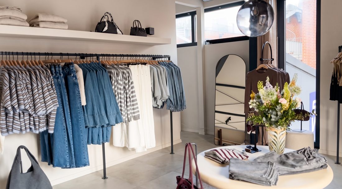 Kleiderstangen mit Jeans und Sommerwei&szlig;, vorn der runde Tisch mit Blumen